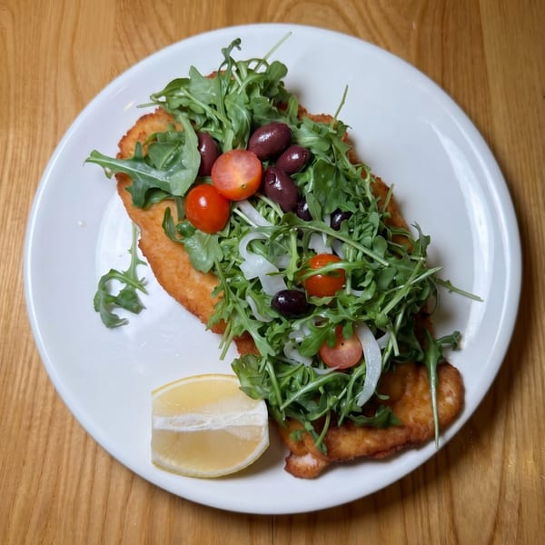 Crispy fried chicken cutlet topped with arugula, cherry tomatoes, olives, onions, and a lemon wedge.