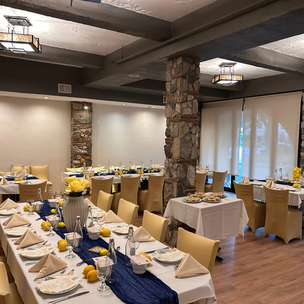A restaurant dining room with tables set with blue runners, lemons, and yellow floral centerpieces.
