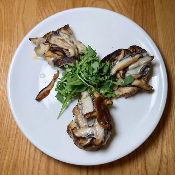 Three pieces of toast topped with mushrooms, melted cheese, and a pile of arugula on a white plate.