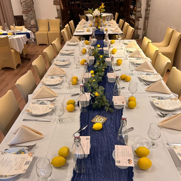 Long dining tables set with white tablecloths, blue runners, lemons, and Limoncello menus.