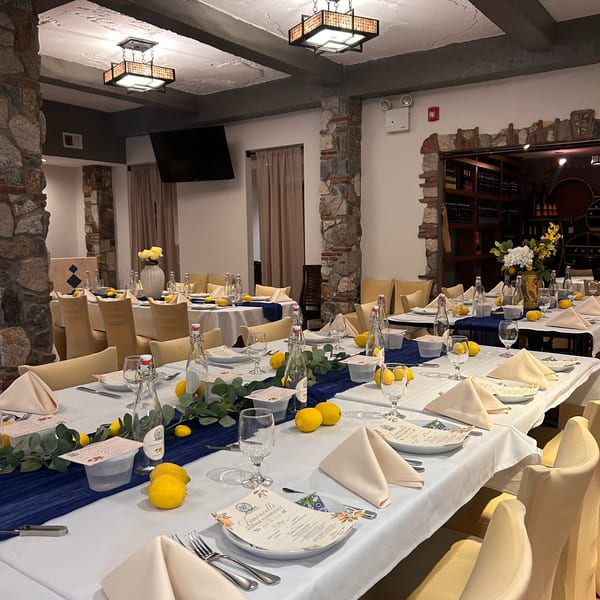 A restaurant dining room with long tables set with white tablecloths, blue runners, lemons, and menus.