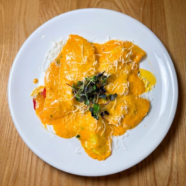 Ravioli with orange sauce, shredded cheese, and microgreens on a white plate.